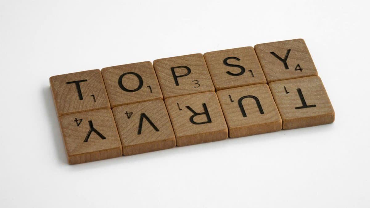 Close-up of wooden Scrabble tiles arranged to spell 'topsy turvy' on a white background.