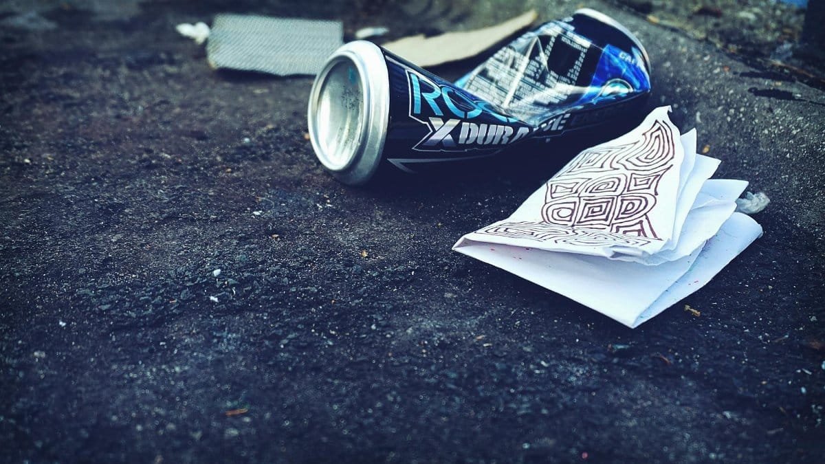 A crumpled beverage can and papers litter an urban street, highlighting environmental issues.