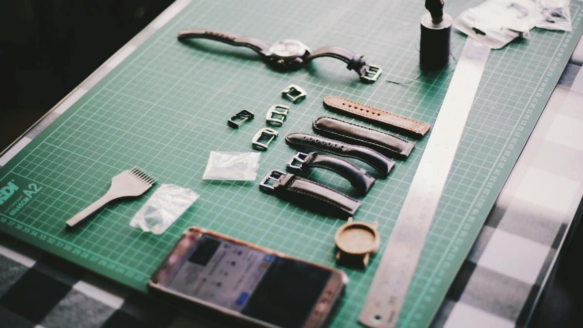 Close-up of watchmaking tools and leather straps on a crafting table.