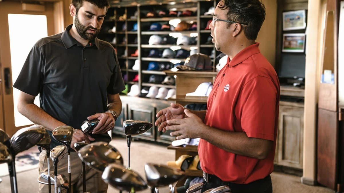 Customer receiving expert advice from salesman on golf equipment in a store.