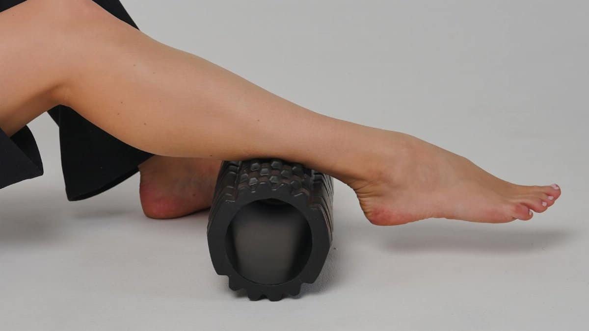 Close-up of a leg using a foam roller for stretching and muscle relief in a studio setting.