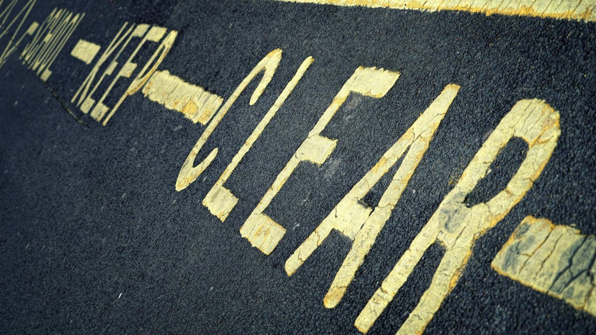 Close-up of yellow road markings with 'KEEP CLEAR' instruction on asphalt surface.