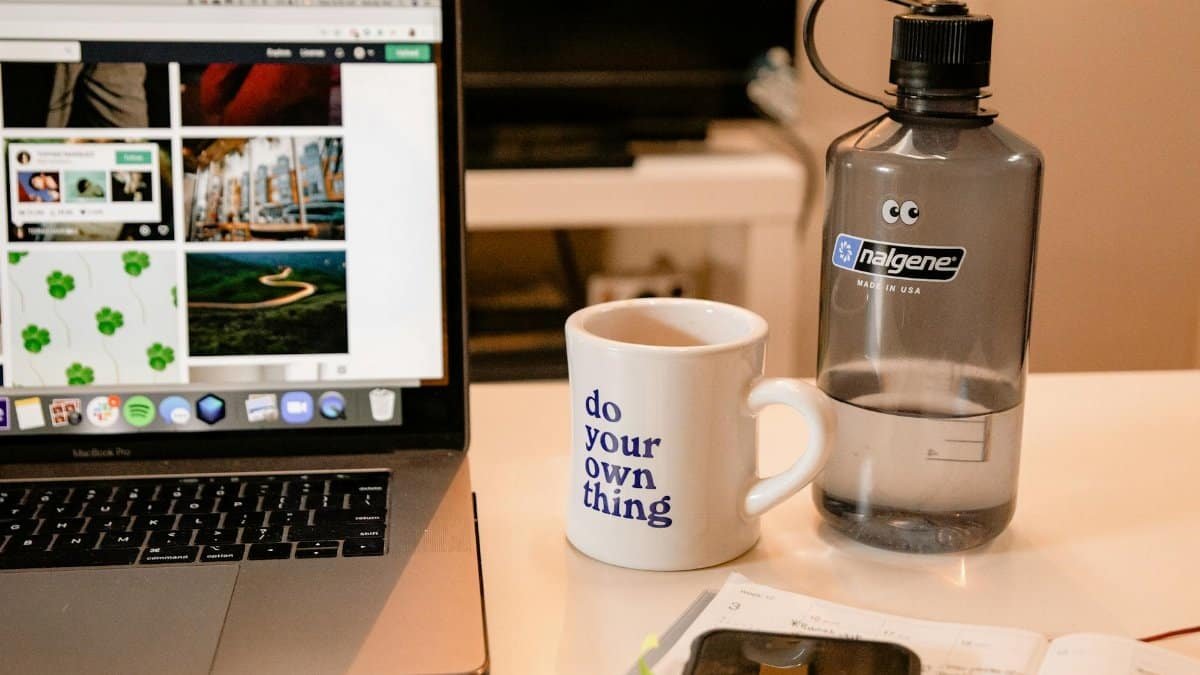 Cozy workspace with laptop, motivational mug, and water bottle, perfect for remote work inspiration.
