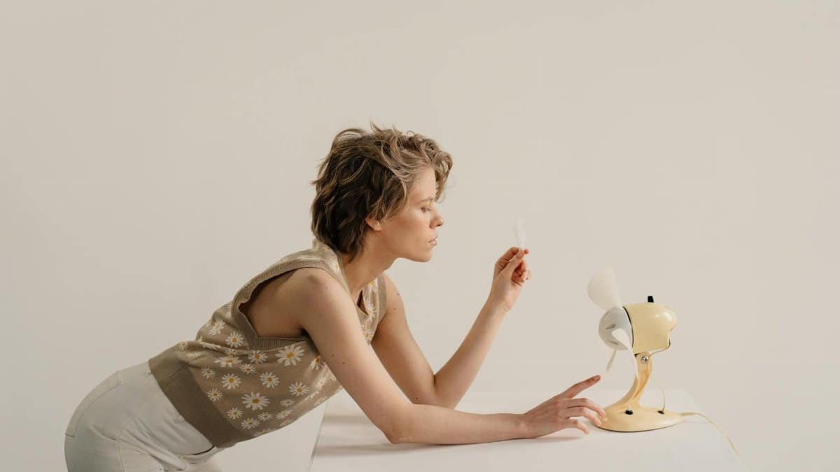 Adult woman leaning over table testing airflow with a desk fan indoors.