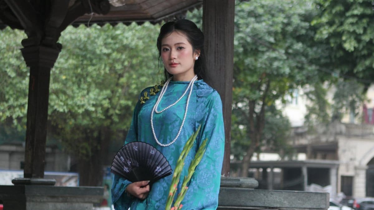 Woman in blue traditional attire holding a fan in an outdoor setting.