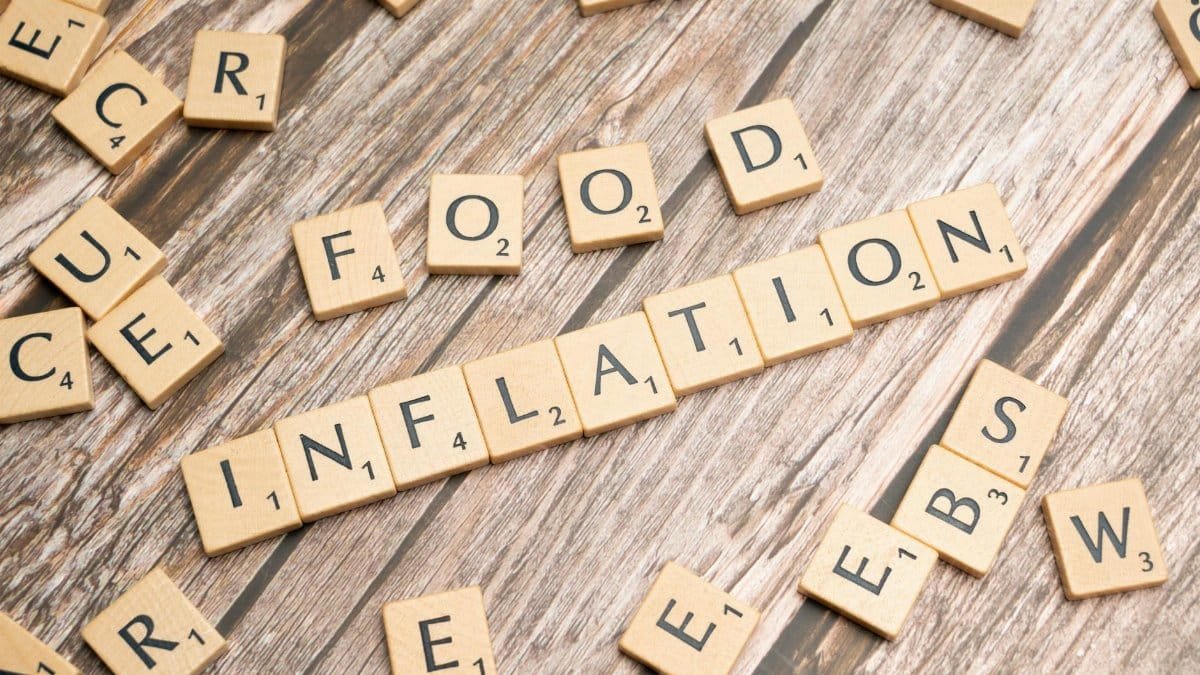 Wooden scrabble tiles arrange to spell 'Food Inflation' on a rustic wooden surface, conceptually depicting rising food prices.