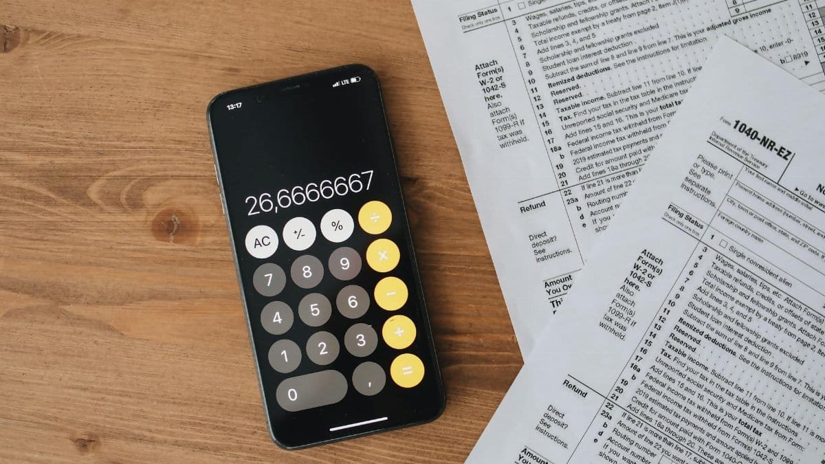 Overhead view of smartphone calculator and tax forms on a wooden table.