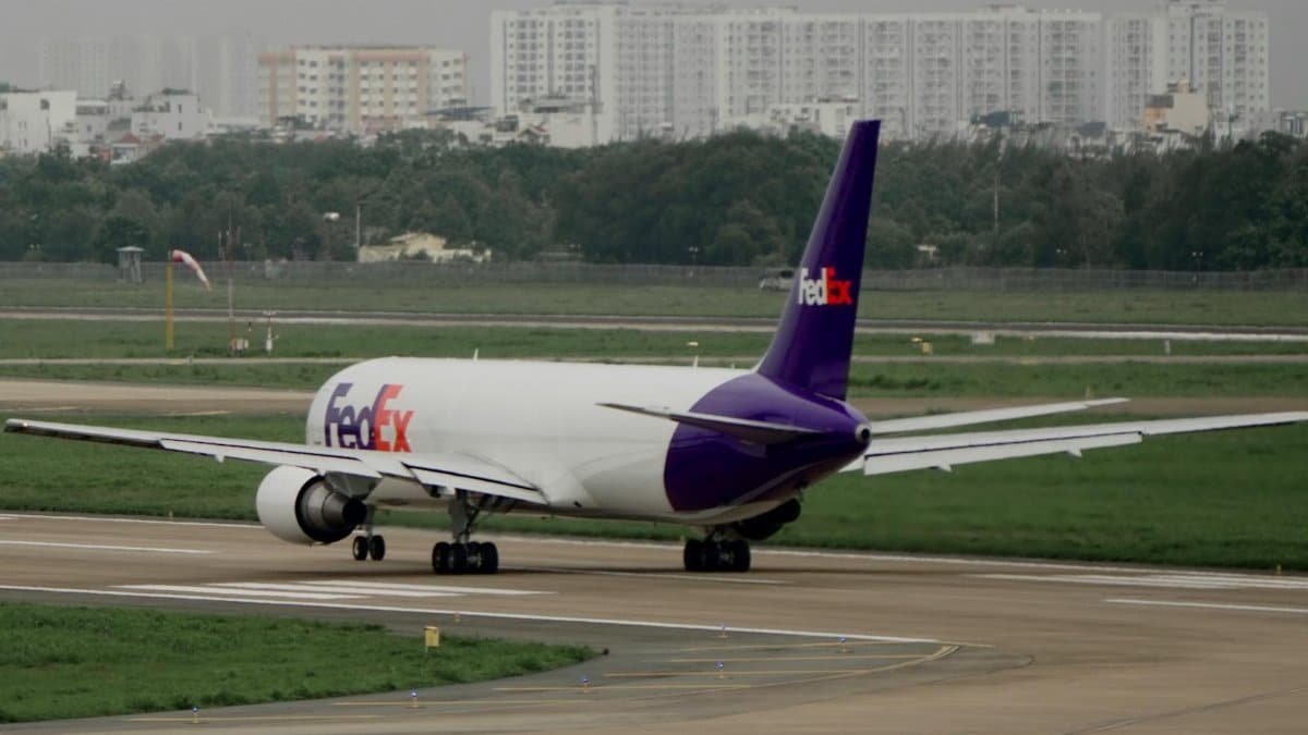 FedEx cargo plane on the runway, preparing for departure with cityscape in the background.