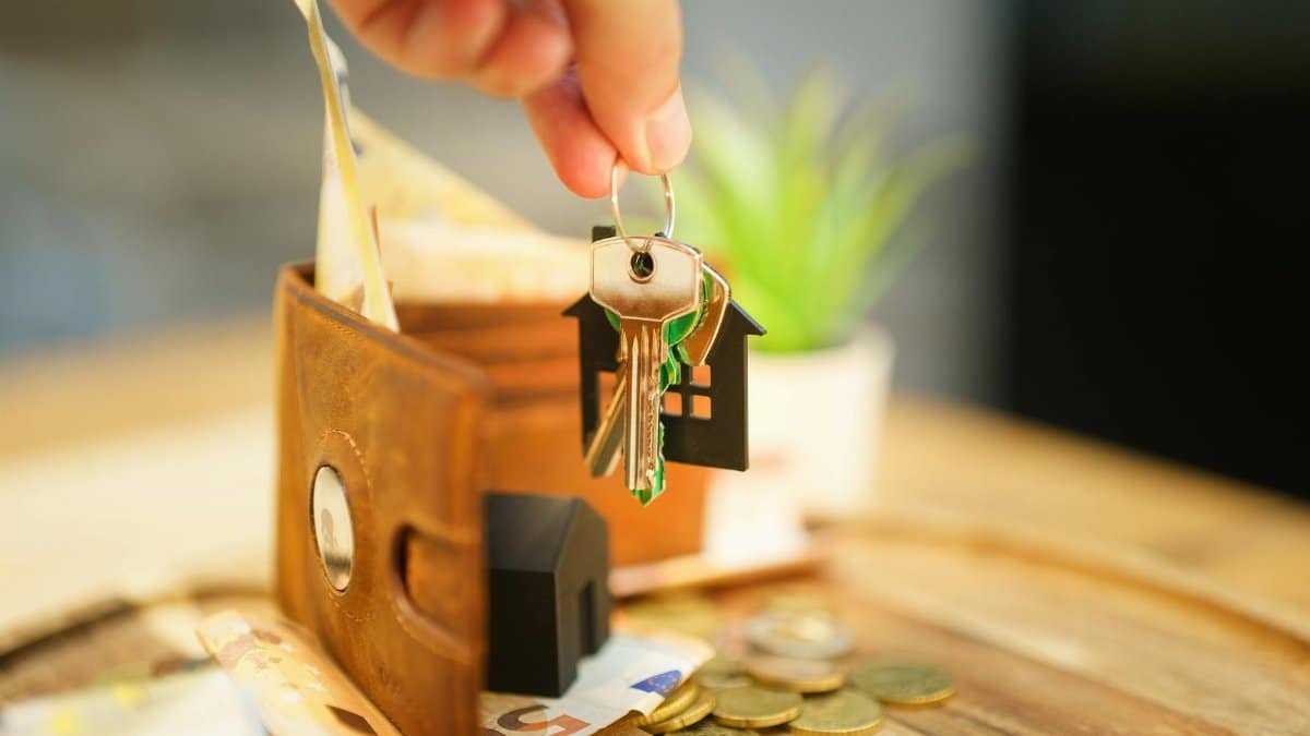 Close-up of hand holding a house key with a wallet and coins, symbolizing real estate investment.