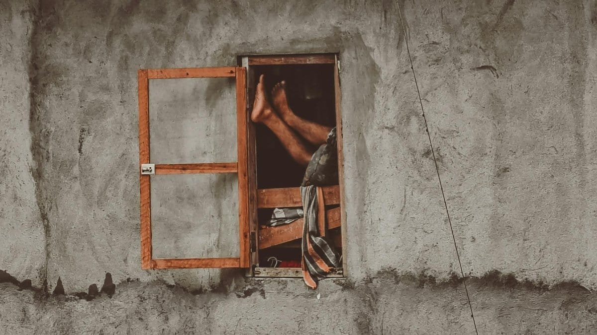 A person lounging barefoot, legs extended through an open window of a concrete wall.