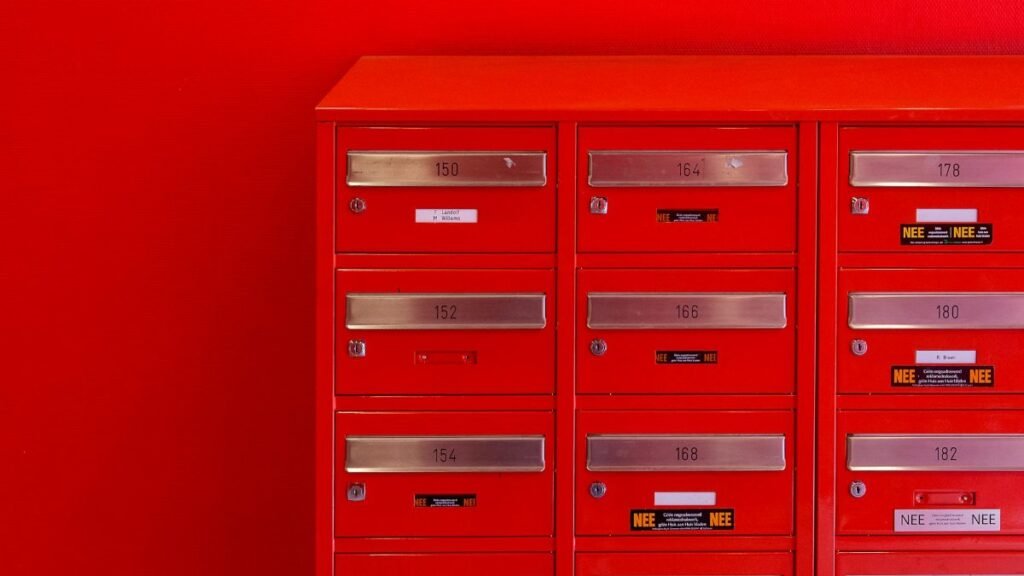 A row of sleek red mailboxes with metallic number panels and keyholes against a red background.