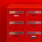 A row of sleek red mailboxes with metallic number panels and keyholes against a red background.