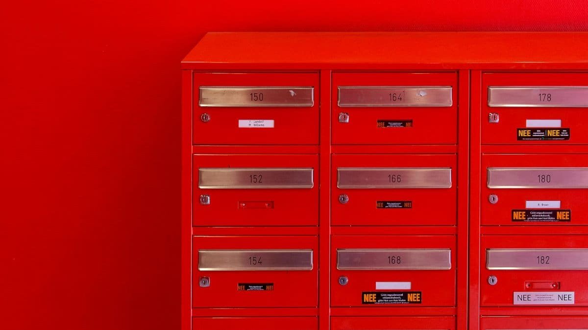 A row of sleek red mailboxes with metallic number panels and keyholes against a red background.