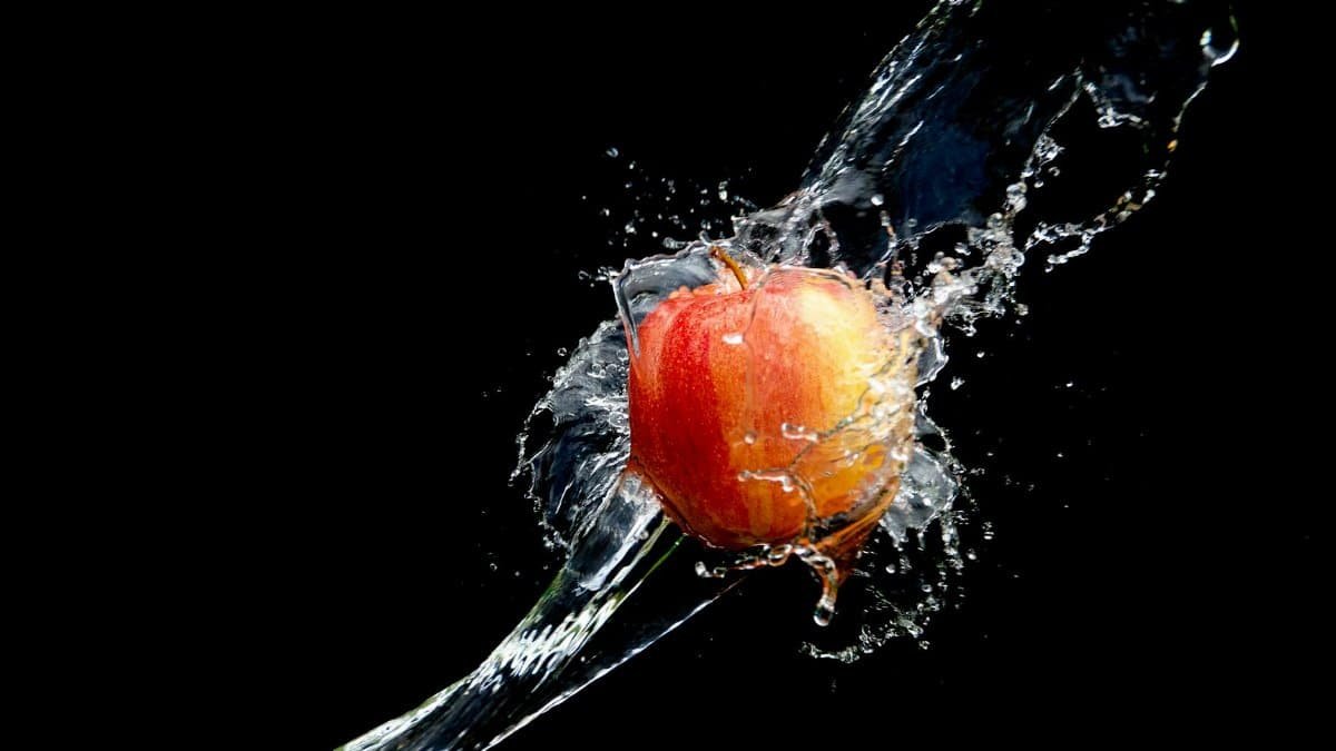 A fresh apple splashes through water against a solid black background, highlighting its vibrant colors.