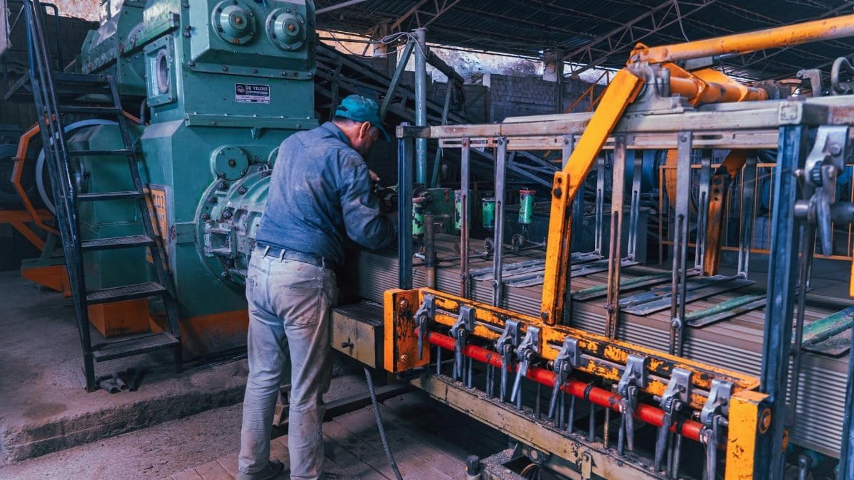 A factory worker operates heavy machinery in an industrial setting, depicting a typical manufacturing scene.