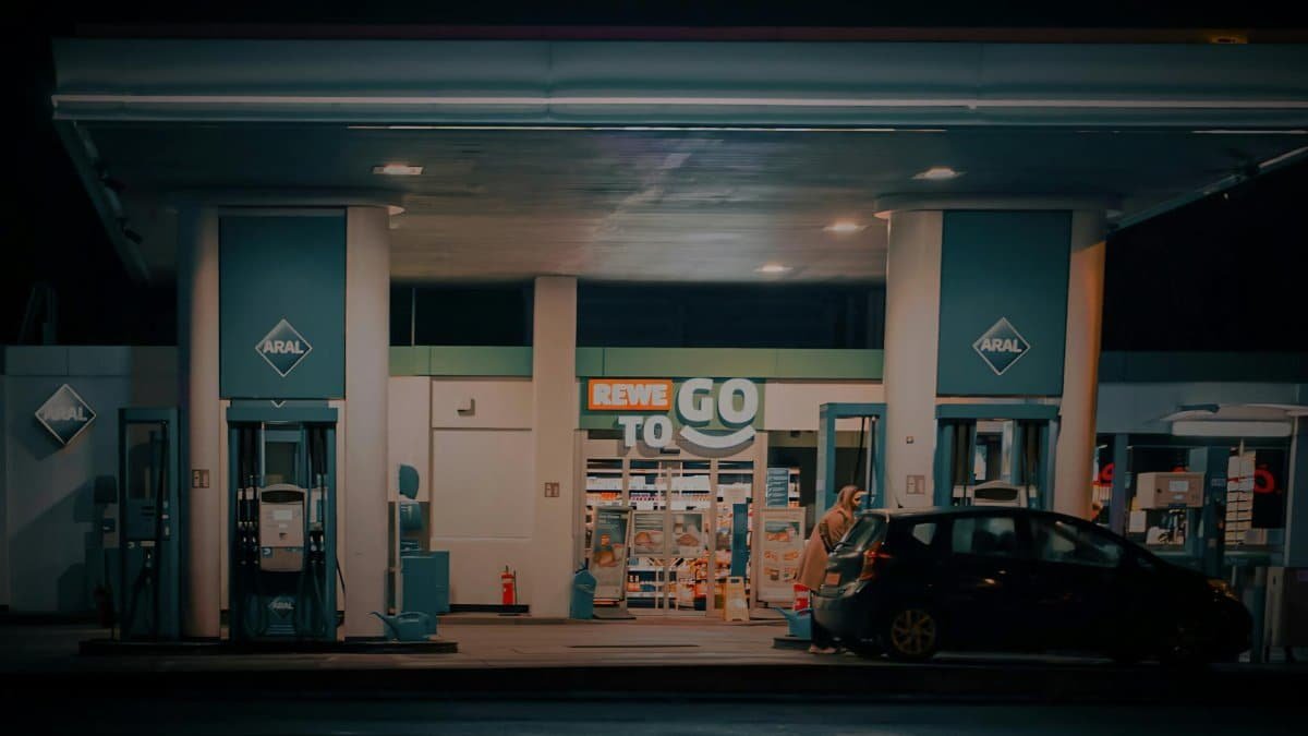 A nighttime view of a gas station and convenience store with a car parked at the pump.