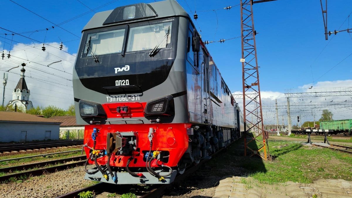 A modern freight train parked on railway tracks under a clear blue sky.