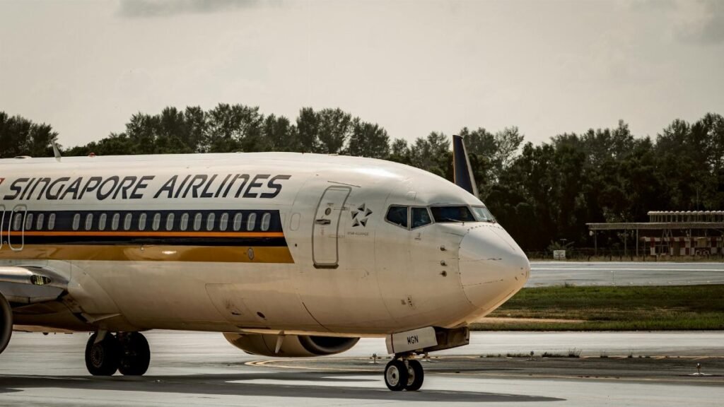 Singapore Airlines plane taxiing on airport runway under cloudy skies.