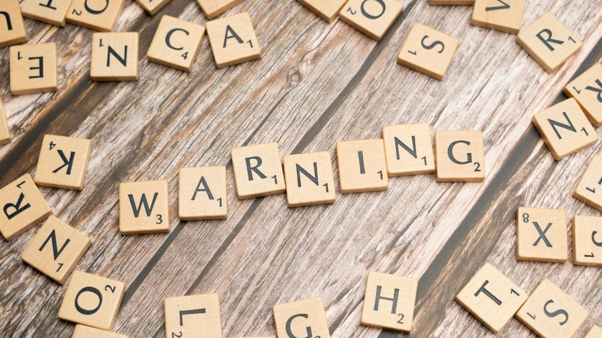 Wooden letter tiles forming the word 'Warning' on a rustic wooden surface.
