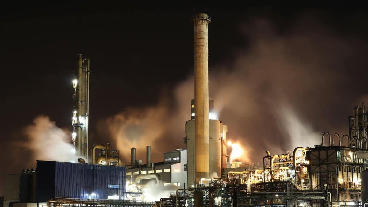 A nighttime view of an industrial factory with smokestacks emitting smoke, highlighting energy production and pollution.
