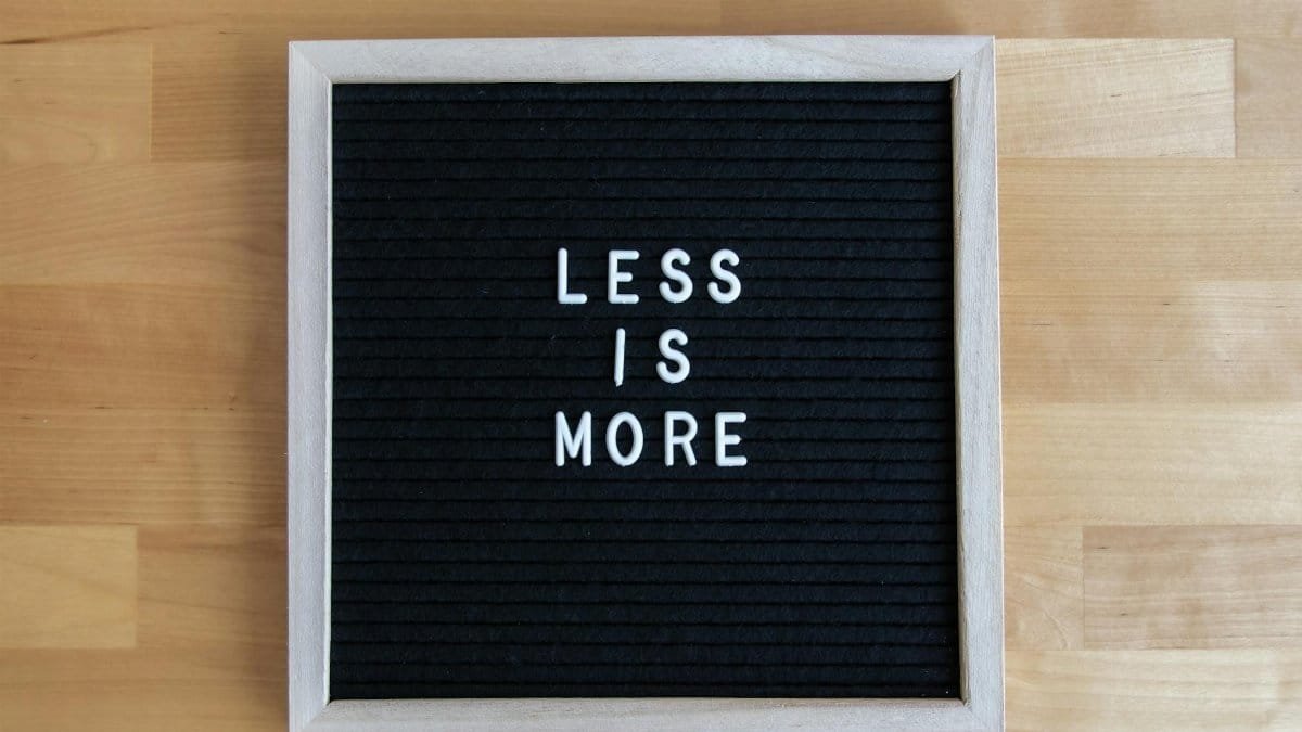 A black letter board with white letters spelling 'Less is More' on a wooden table.