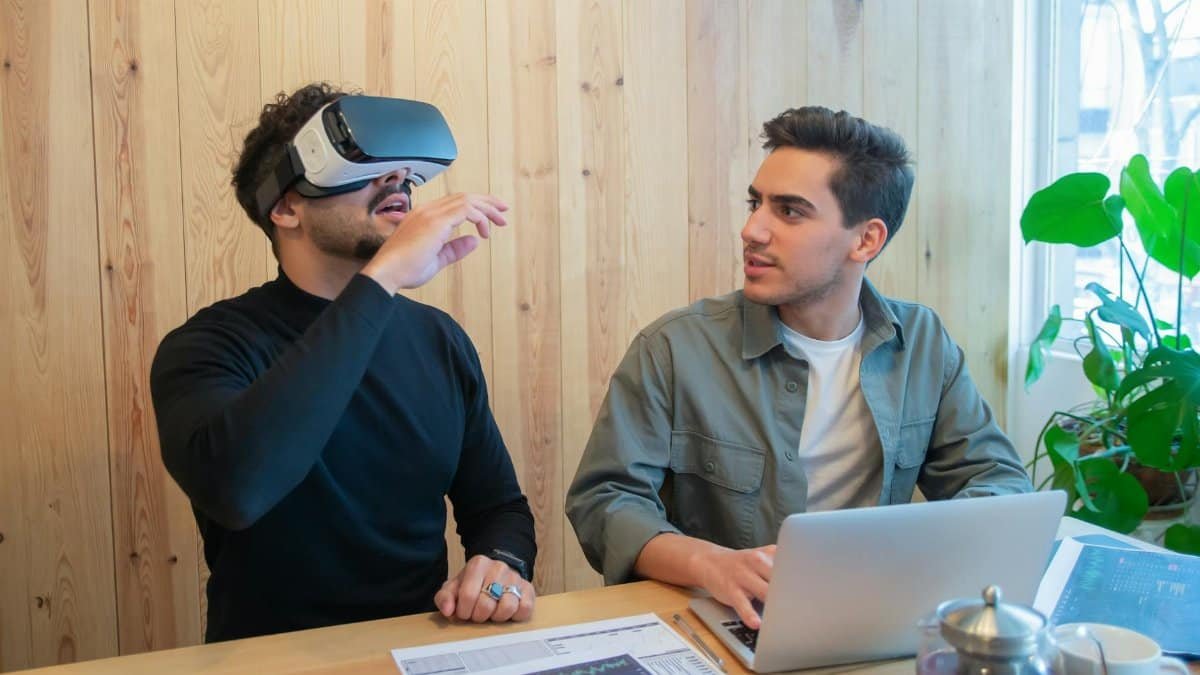 Two colleagues engage in a tech-savvy business meeting using virtual reality and laptops indoors.
