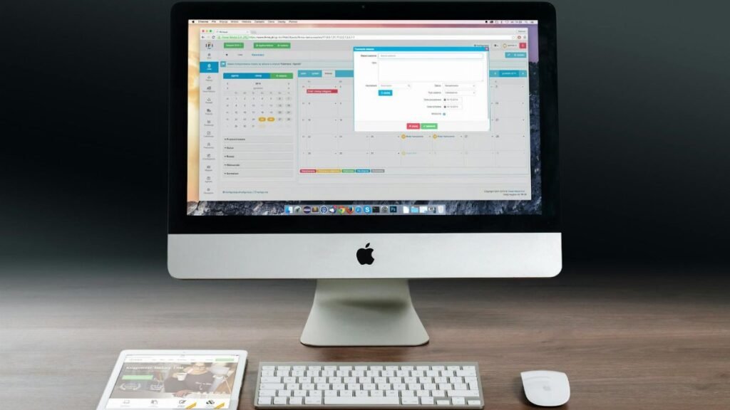 A sleek office setup featuring an Apple iMac, iPad, and keyboard on a wooden desk.