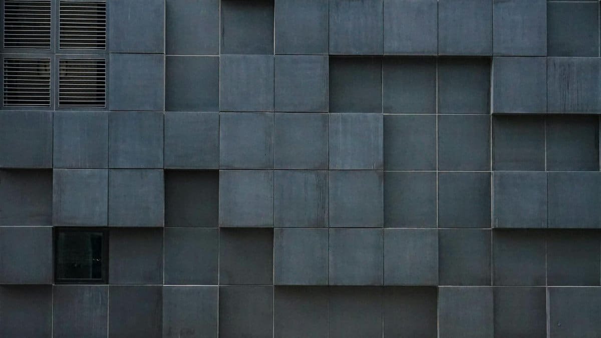 Close-up of a modern building facade with grey geometric tiles and vent panels.