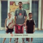 Tennis coach with two young players indoors at Vibora Club.