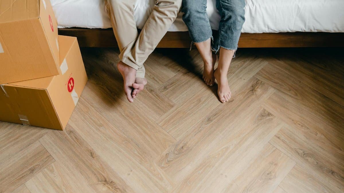 Unrecognizable barefoot man and woman sitting on bed near carton boxes while relaxing from unboxing belongings during relocation in new flat