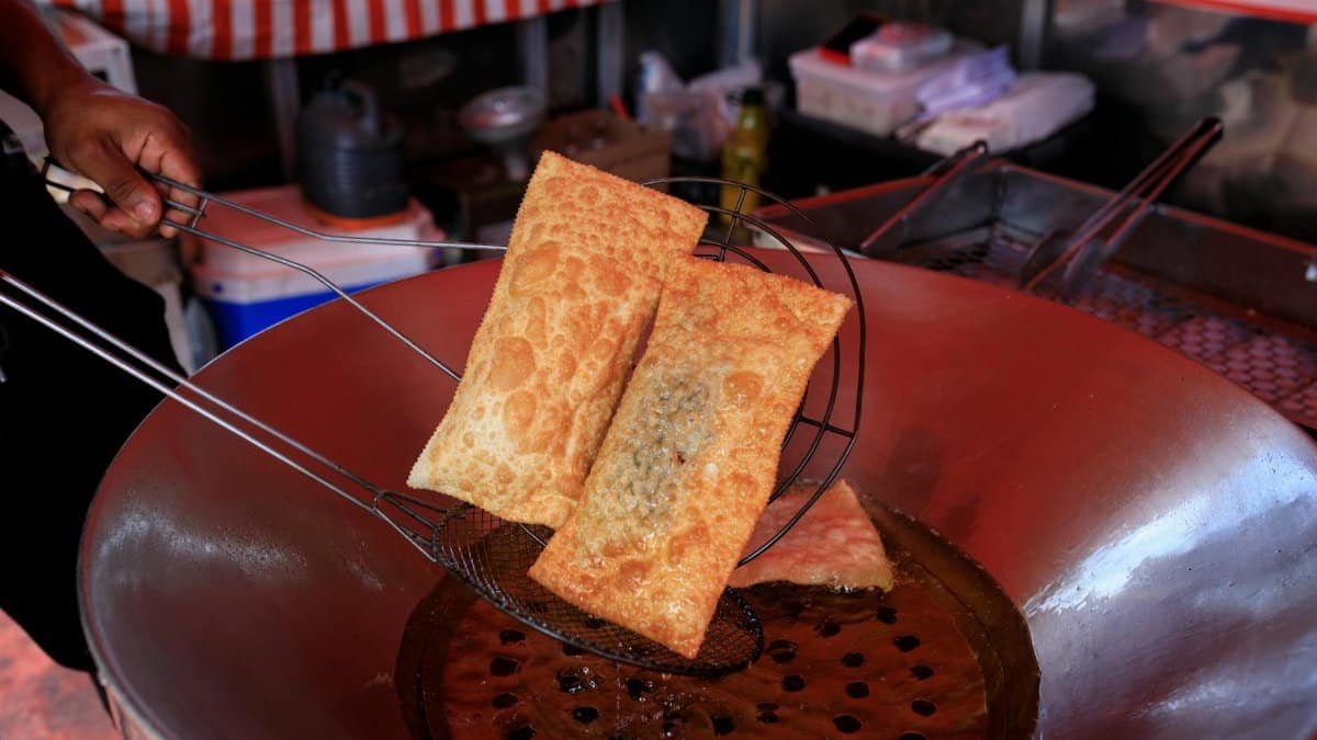 Freshly fried crispy pastries in hot oil, showcasing vibrant street food culture.