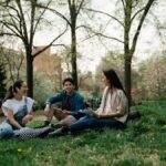 Group of college students sitting and chatting on the grass in a park during spring.