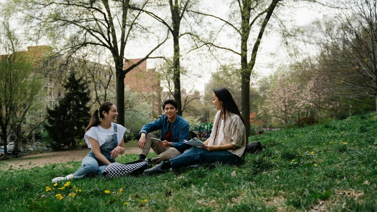 Group of college students sitting and chatting on the grass in a park during spring.