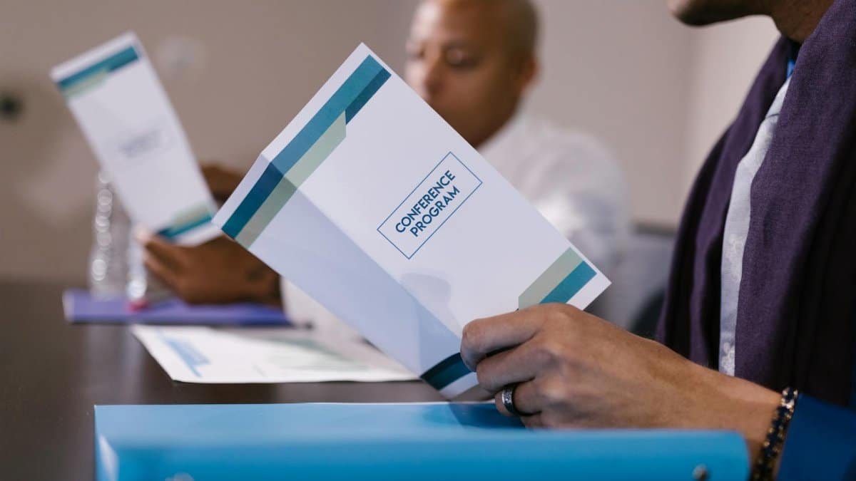 Close-up view of attendees reading conference programs during a business meeting.