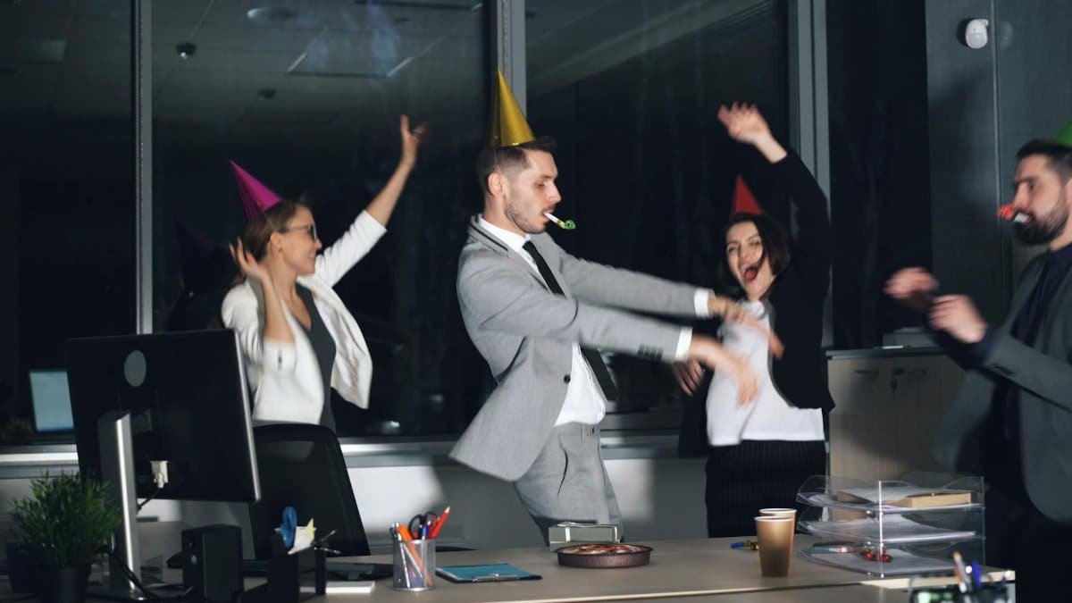 Happy office workers celebrating with party hats and blowouts in a lively indoor setting.