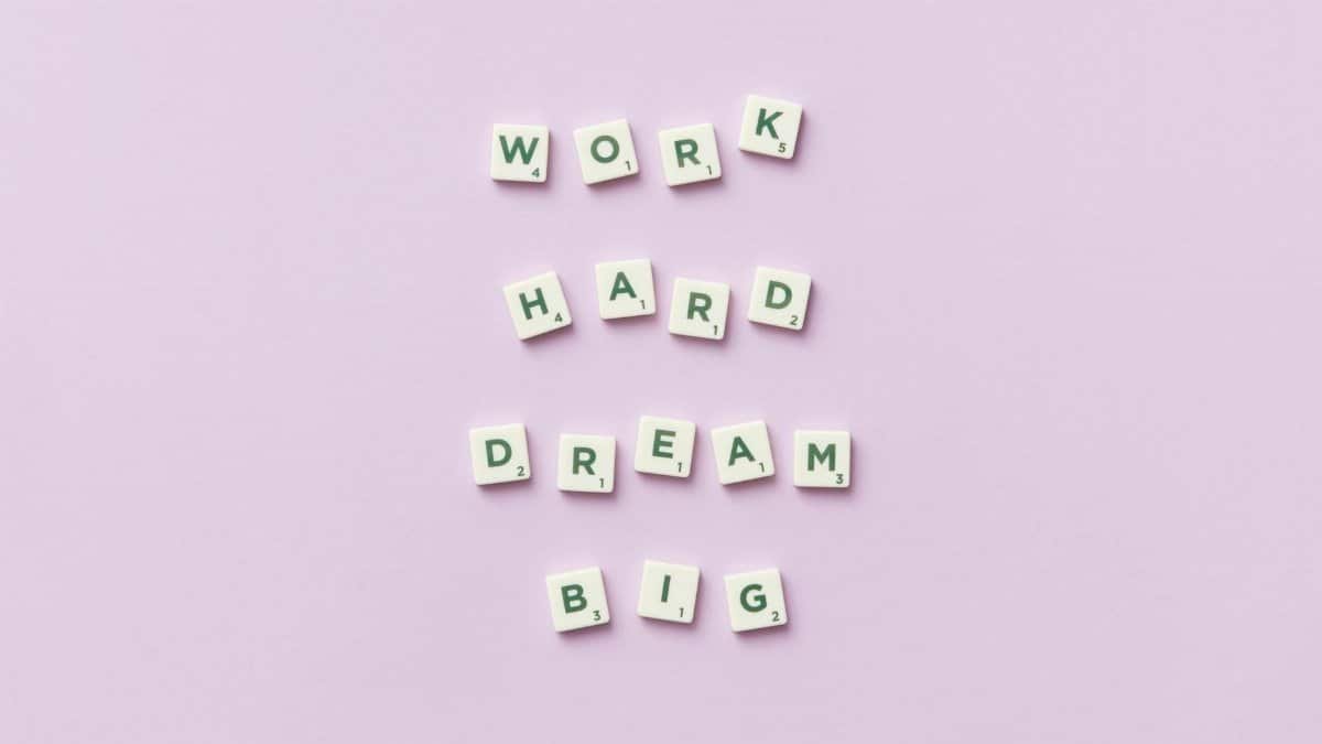 Scrabble tiles spell 'Work Hard Dream Big' on a pastel purple surface, top view.