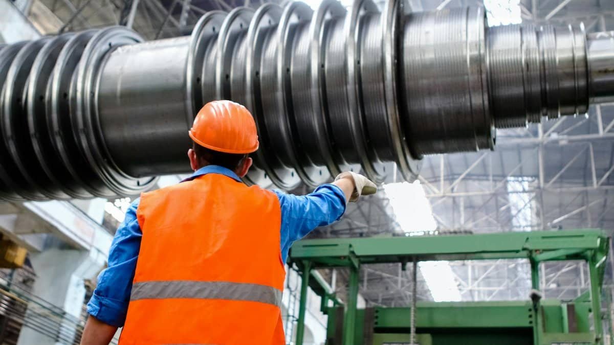 Engineer in high visibility vest and hard hat inspecting large machinery in factory setting.
