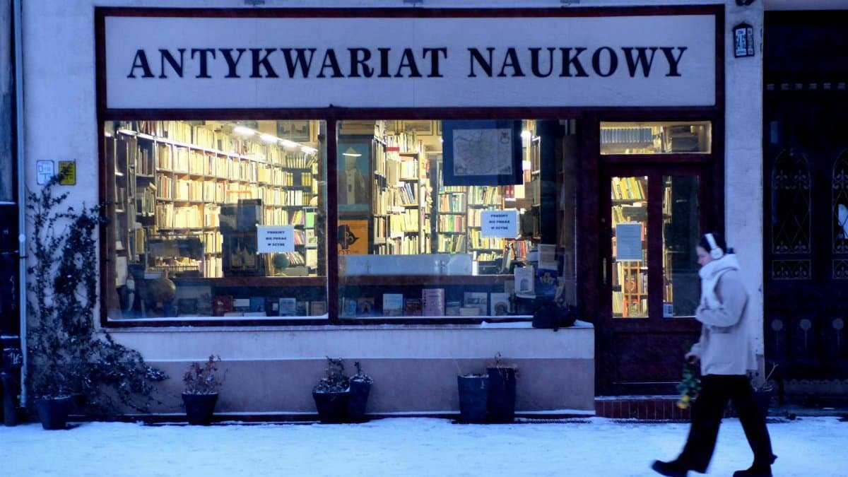 A person walks by a vintage bookstore named 'Antykwariat Naukowy' in a snowy European street.