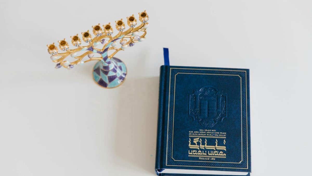 An ornate menorah and a Hebrew book on a white surface, perfect for Hanukkah themes.