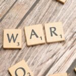 Close-up of wooden scrabble tiles spelling 'WAR' on a wooden background.