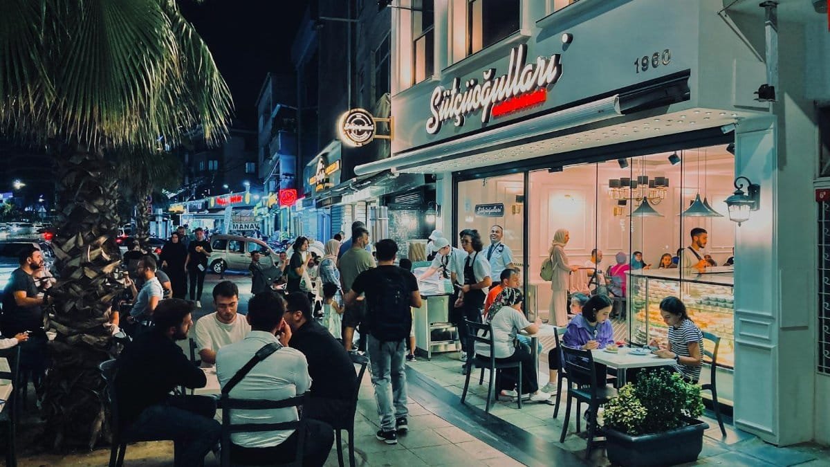 Nighttime scene at a bustling sidewalk cafe in Istanbul, Turkey, featuring diverse people enjoying the urban nightlife.