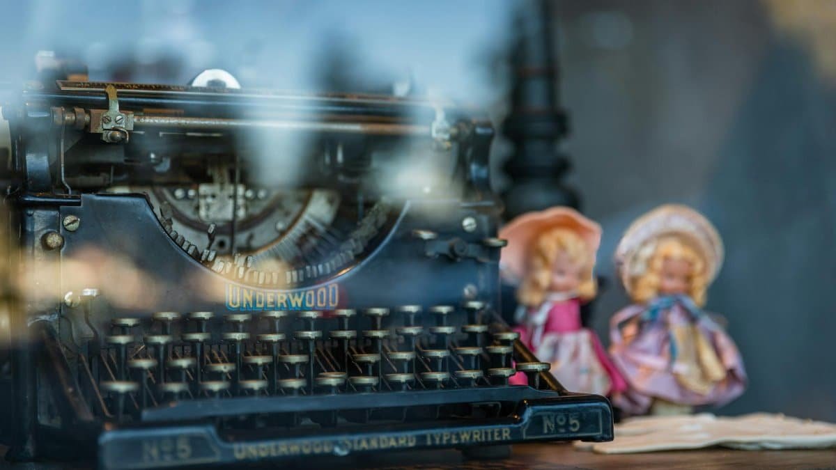 An antique Underwood typewriter with vintage dolls reflected in a window display.