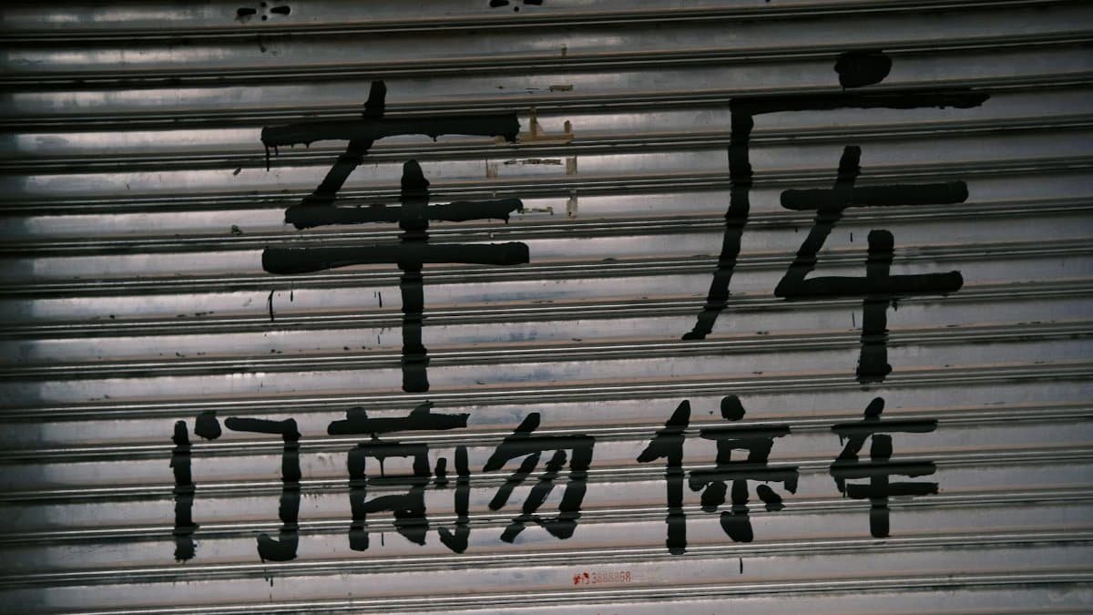 Graffiti in bold Chinese characters on a closed metal shutter in an urban area.