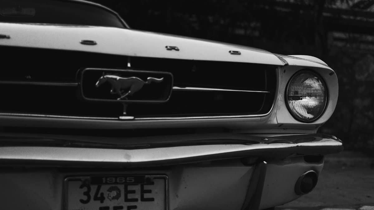 Grayscale image of a classic 1965 Ford Mustang with focus on the car's front grille and emblem.