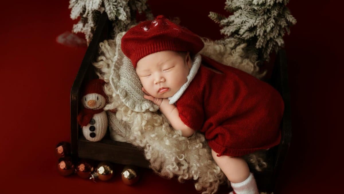 A cute newborn baby in red clothing, peacefully sleeping in a cozy holiday setting with Christmas decorations.