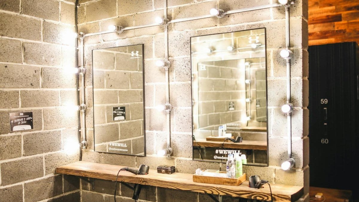 Industrial-style bathroom featuring a well-lit vanity mirror with exposed bulbs and concrete walls.