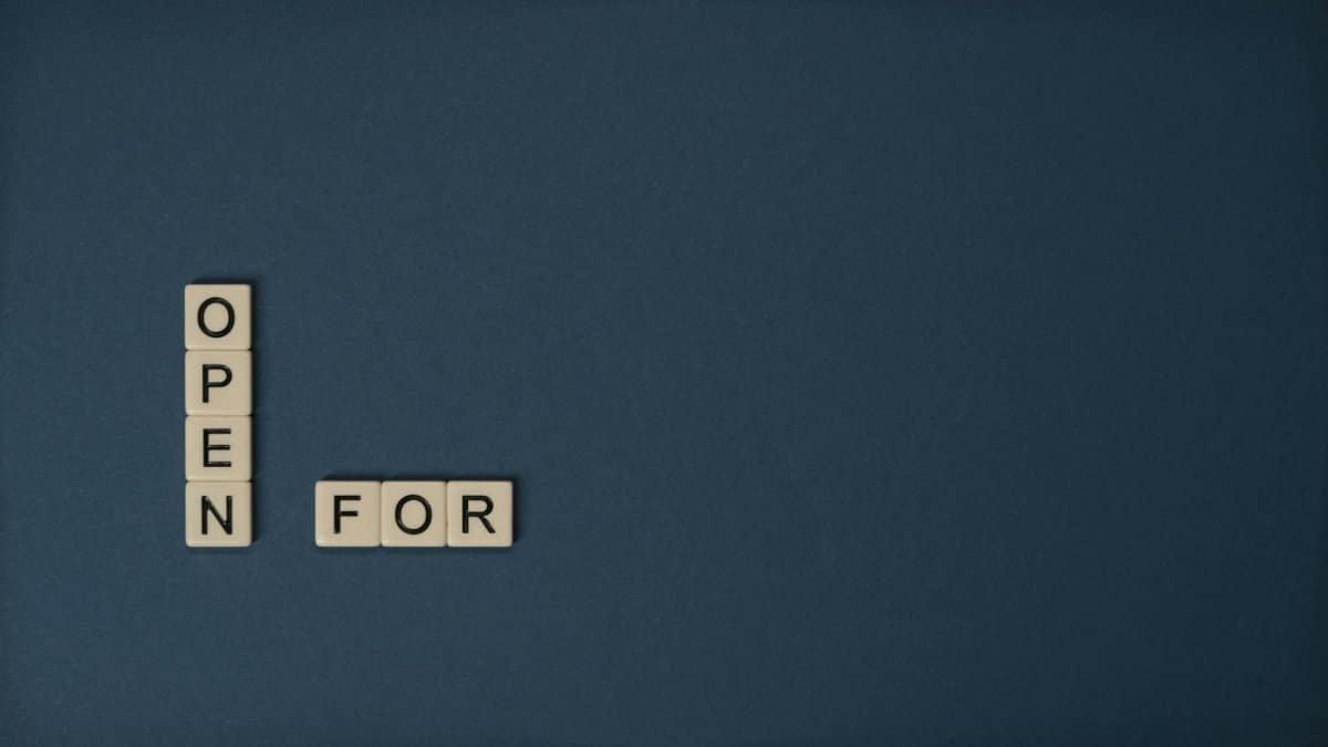 Scrabble tiles forming text 'open for' on a blue background with copy space.