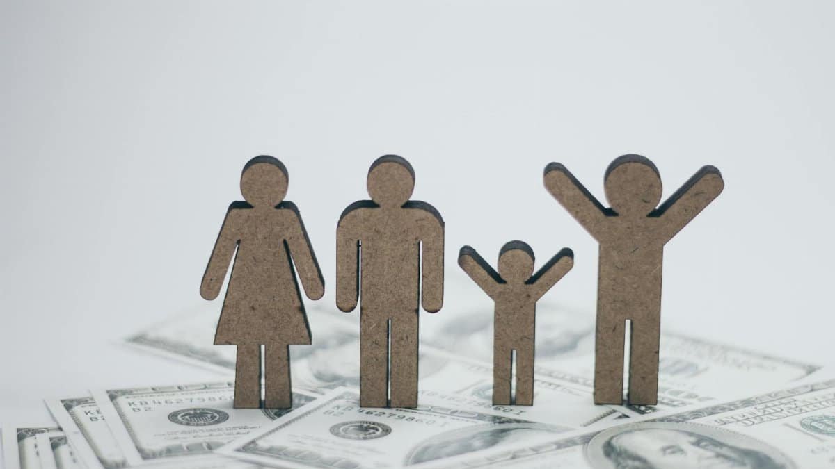 Wooden family figurines on dollar bills symbolizing financial stability.