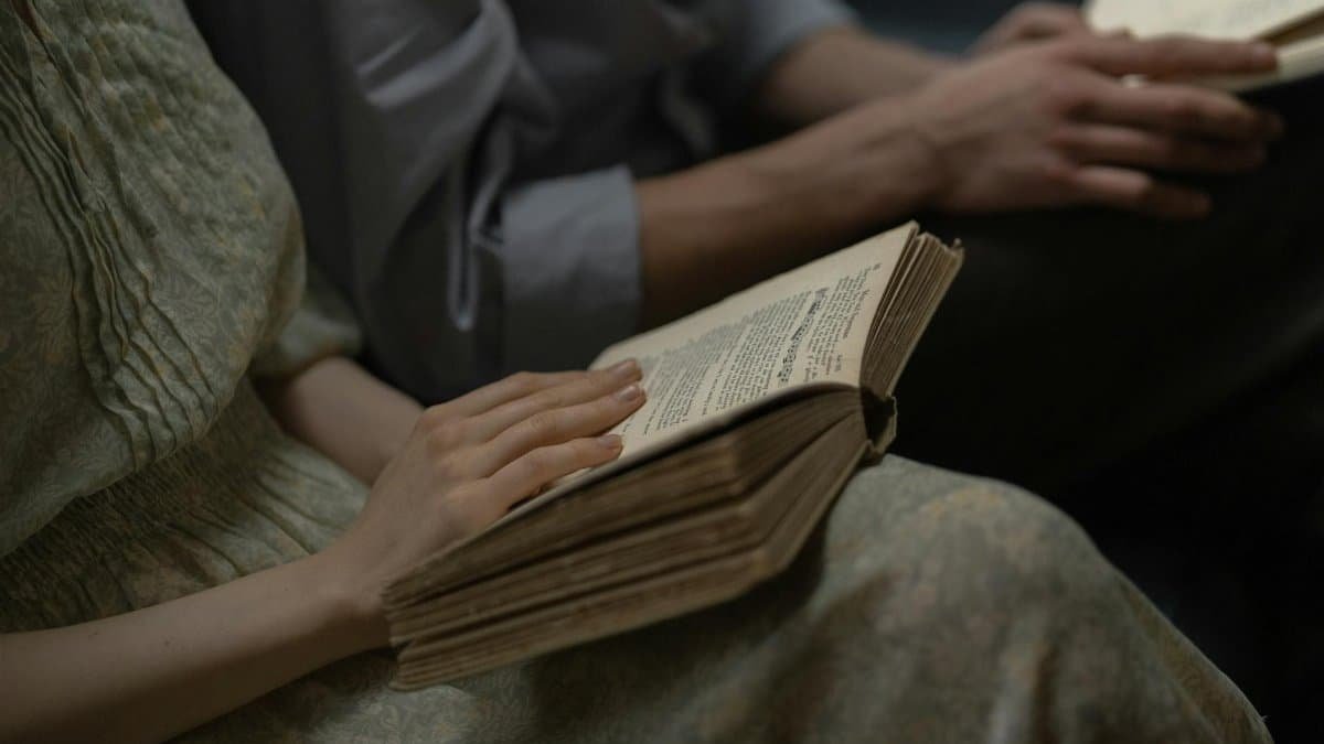 Close-up of two people reading an antique book, focusing on the hands and text.
