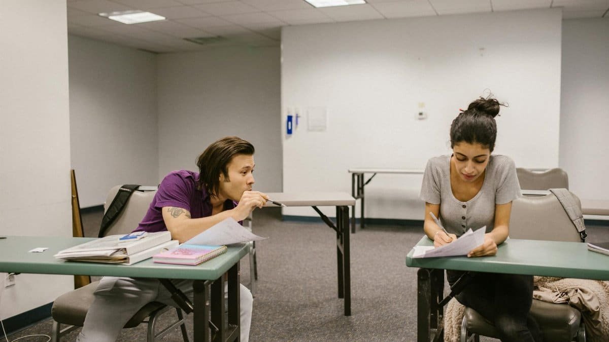 Two college students in a classroom setting, one appears to be copying from the other's paper.